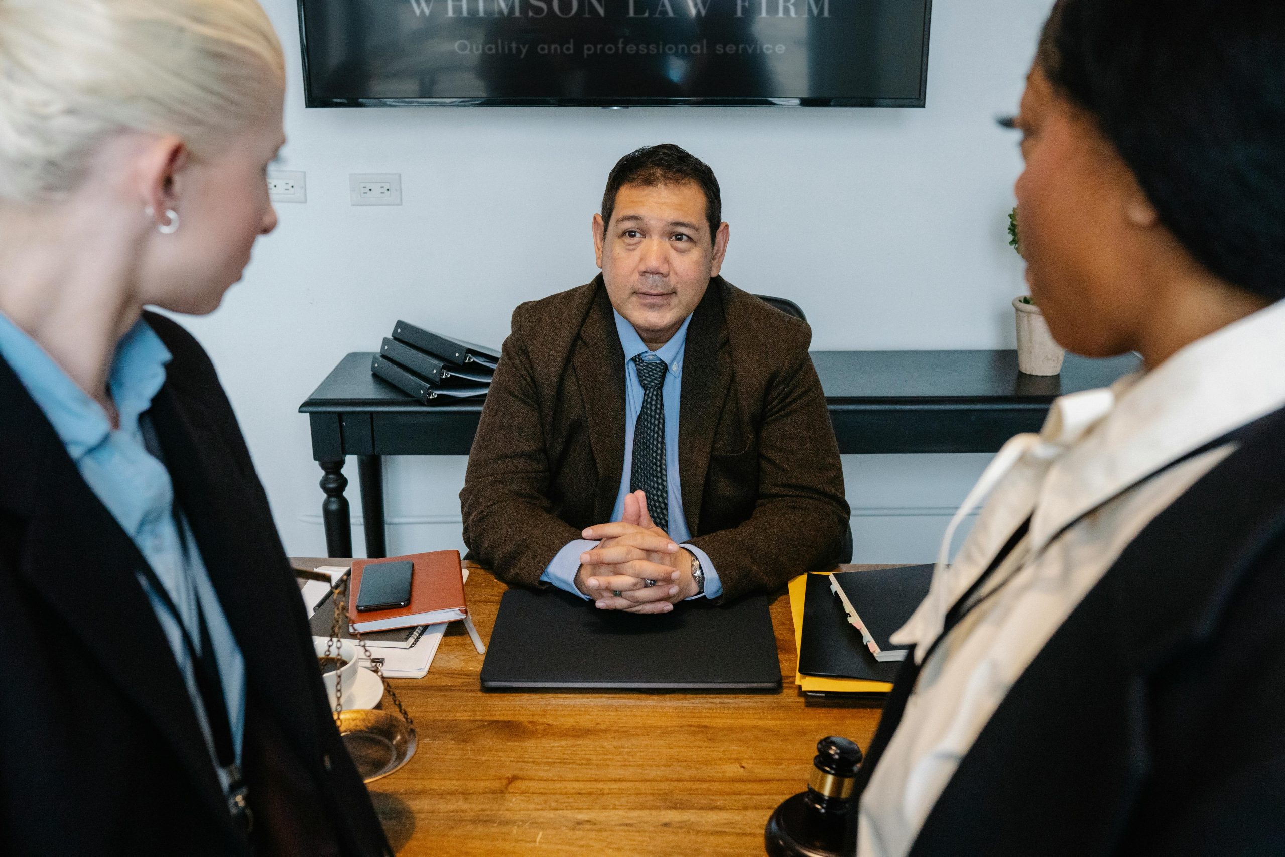 Three diverse attorneys in a formal meeting at a law firm office table.