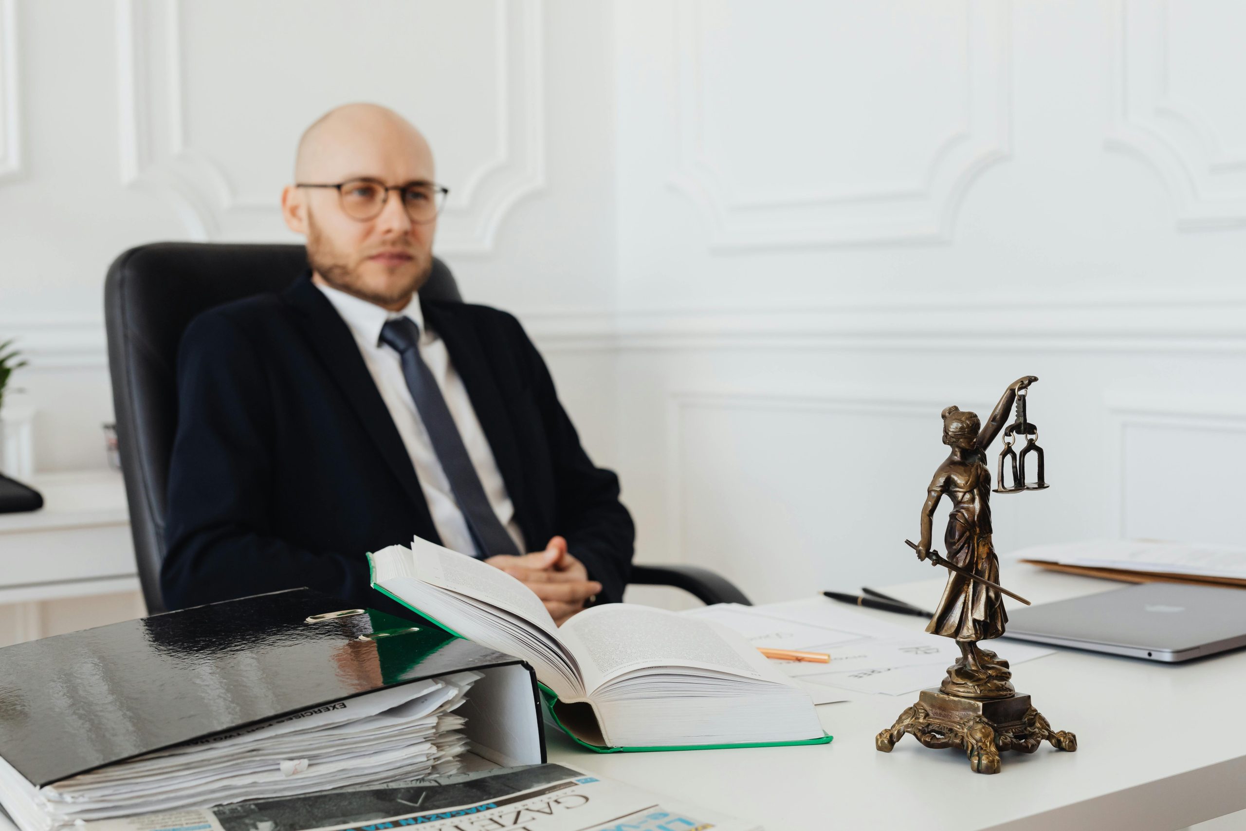 Bald lawyer in office sitting with legal documents and Justice statue.