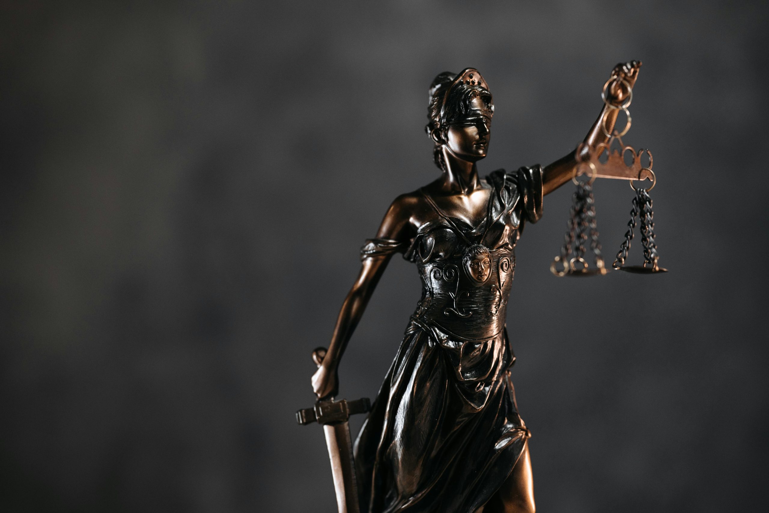 Detailed bronze Lady Justice statue with scales and sword against a dark background, symbolizing law and justice.